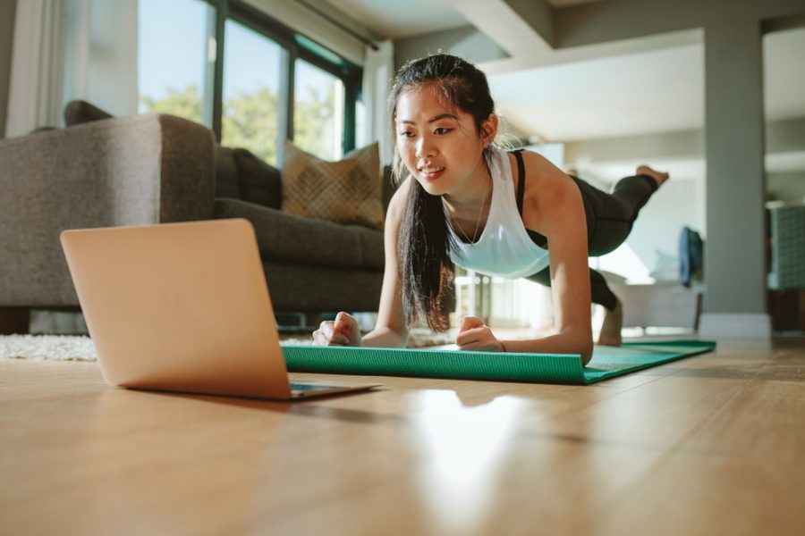 Woman working out at home watching video tutorial on laptop. Fit young woman in plank position repeating online instructions by coach on computer.