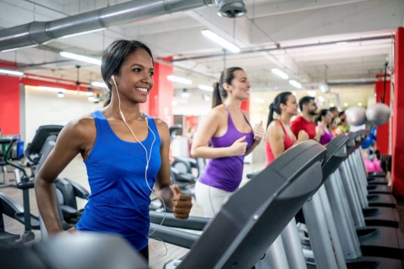 Happy group of people running on the treadmills at the gym and smiling â fitness concepts